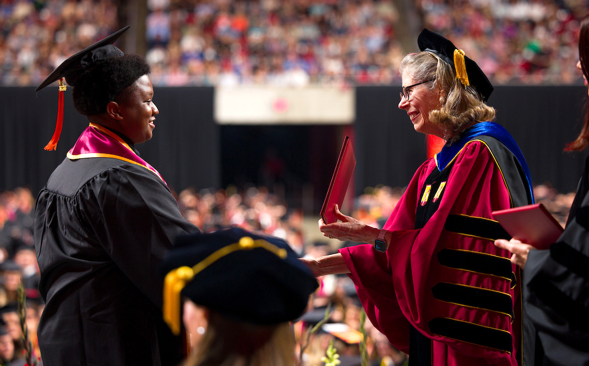 Wendy Wintersteen in academic garb shakes hands with Black male